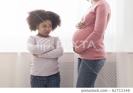 Offended little black daughter looking at pregnant mom's belly with jealousy Offended little black daughter looking at pregnant mom's belly with jealousy 62711348