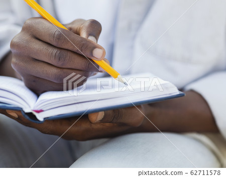 Close up of afro student taking notes, using notepad and pencil Close up of afro student taking notes, using notepad and pencil 62711578