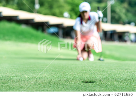 Young professional female golf player crouching and study the green before putting shot,she does exercise for relax time 62711680