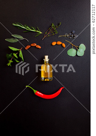 Smiling face making from herbs and bottle of essential oil on black background, top view, flat lay 62712117
