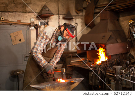 The blacksmith forging the molten metal on the anvil in smithy. The blacksmith forging the molten metal on the anvil in smithy. 62712143