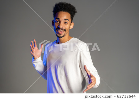 Young very active and energetic african american man in white wear smiling and dancing in good mood on grey background Young very active and energetic african american man in white wear smiling and dancing in good mood on grey background 62712644