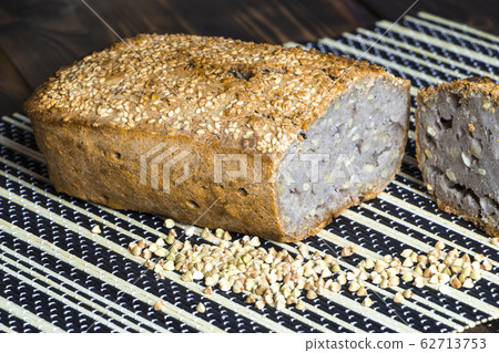 Vegan buckwheat bread. Freshly baked traditional bread on a bamboo serving mat on wooden table. Scattered grains and a slice near it. Selective focus. Healthy eating. Homemade natural food 62713753