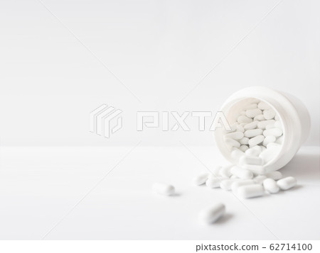 White pills spilled out of a plastic jar. Medicine capsules on white background with copy space. White pills spilled out of a plastic jar. Medicine capsules on white background with copy space. 62714100