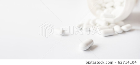 White pills spilled out of a plastic jar. Medicine capsules on white background with copy space. White pills spilled out of a plastic jar. Medicine capsules on white background with copy space. 62714104
