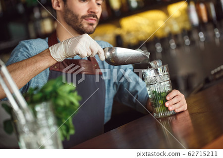 Making Drink. Bartender standing at counter adding ice inro glass concentrated close-up 62715211