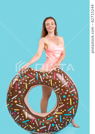 Summer Freestyle. Young woman with freckles standing isolated on blue posing with swim ring smiling cheerful Summer Freestyle. Young woman with freckles standing isolated on blue posing with swim ring smiling cheerful 62715244