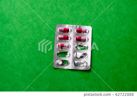Pack of red and white medicine capsules on a green Pack of red and white medicine capsules on a green 62722888