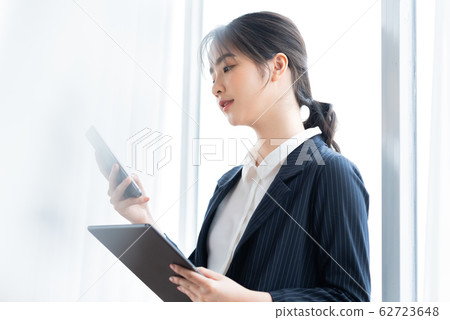 A business womaA business woman using tablet beside the windown using smartphone beside the window A business womaA business woman using tablet beside the windown using smartphone beside the window 62723648