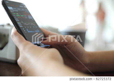Female hand with smartphone trading stock online in coffee shop , Business concept Female hand with smartphone trading stock online in coffee shop , Business concept 62725372