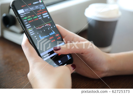 Female hand with smartphone trading stock online in coffee shop , Business concept Female hand with smartphone trading stock online in coffee shop , Business concept 62725373