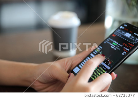 Female hand with smartphone trading stock online in coffee shop , Business concept Female hand with smartphone trading stock online in coffee shop , Business concept 62725377