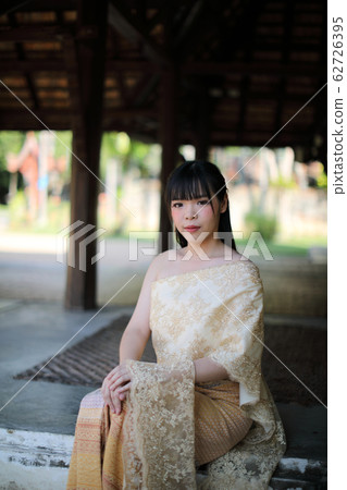 Portrait of Thai female with traditional Thai dress sitting with temple background 62726395