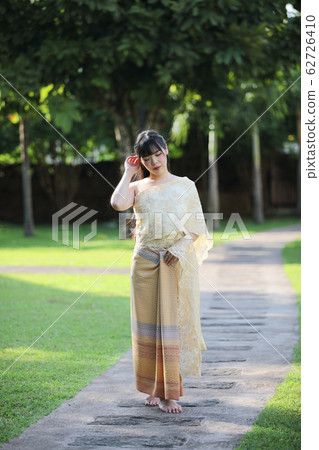 Portrait of Thai female with traditional Thai dress walking with temple background 62726410