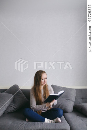 Smart young female sitting on the couch at home reading book 62726825