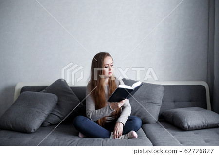 Smart young female sitting on the couch at home reading book 62726827