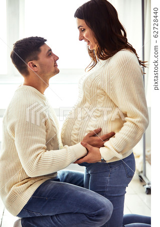 Close up portrait of expecting teenage couple laughing happily, embracing baby in belly together. Couple dressed in blue and white colors. Close up portrait of expecting teenage couple laughing happily, embracing baby in belly together. Couple dressed in blue and white colors. 62728440