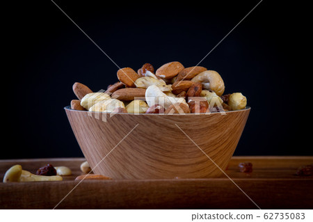 View of white bowl full of variety of nuts on black background 62735083