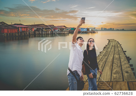 Happy couple taking selfie with cell mobile phone in Chew Jetty fisherman village at sunset. 62736628