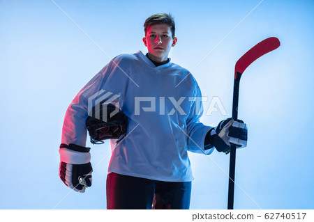Young male hockey player with the stick on ice court and white background in neon light Young male hockey player with the stick on ice court and white background in neon light 62740517
