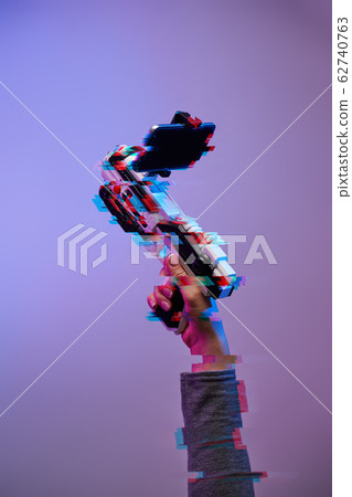 Female hands with a blaster for games with augmented reality on a purple background. Female hands with a blaster for games with augmented reality on a purple background. 62740763