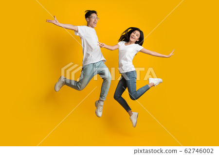 Emotional asian couple jumping over yellow background Emotional asian couple jumping over yellow background 62746002
