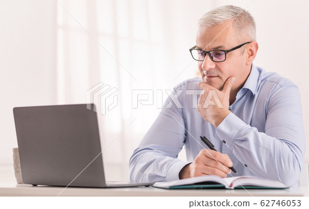 Senior man using laptop at home and writing 62746053
