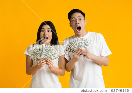 Amazed asian couple holding bunch of money banknotes 62746126