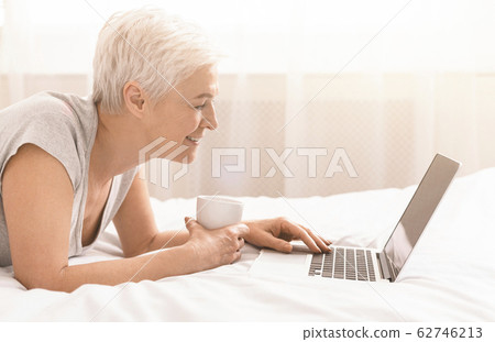 Senior lady browsing on laptop and enjoying morning coffee 62746213