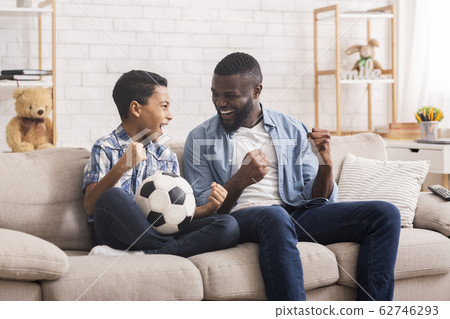 Preteen black boy watching football game on tv with his father Preteen black boy watching football game on tv with his father 62746293