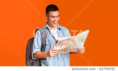 Happy traveler looking at city map over orange background Happy traveler looking at city map over orange background 62746392