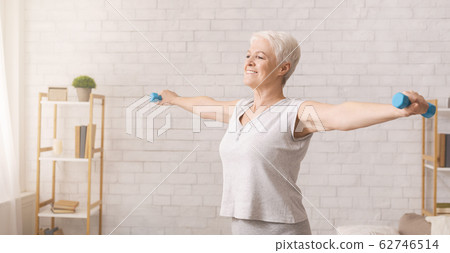 Active senior woman doing exercises with dumbbells at home 62746514