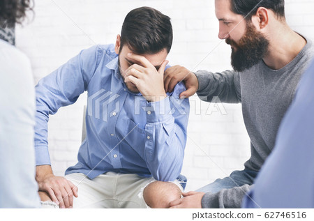 Concerned patients comforting upset man at group therapy session in rehab Concerned patients comforting upset man at group therapy session in rehab 62746516