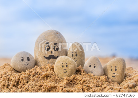 Group of stones with drawn faces in the sand. Group of stones with drawn faces in the sand. 62747160