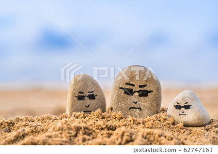 Group of stones with drawn faces in the sand. Group of stones with drawn faces in the sand. 62747161