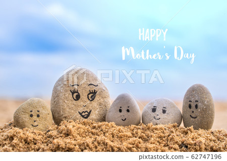 Group of stones with drawn faces in the sand. Group of stones with drawn faces in the sand. 62747196