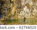Female hiker arrives and admires a waterfall with a beautiful puddle of water 62748020