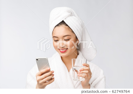 Healthy young beautiful woman drinking water, beauty face natural makeup with holding mobile phone, isolated over white background. 62749764