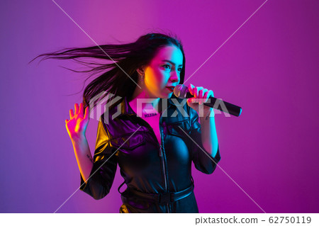Caucasian female singer portrait isolated on purple studio background in neon light Caucasian female singer portrait isolated on purple studio background in neon light 62750119