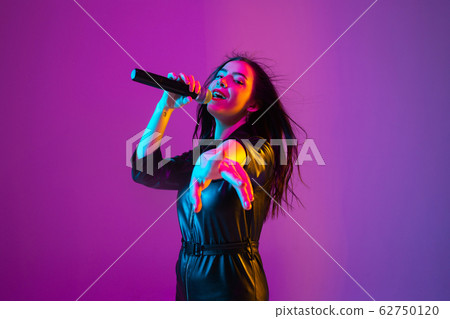 Caucasian female singer portrait isolated on purple studio background in neon light Caucasian female singer portrait isolated on purple studio background in neon light 62750120