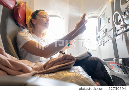 Casual young woman freshening up during airplane flight. Female traveler flying on commercial airplane seated in economy passanger cabin. 62750394