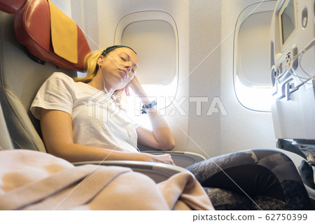 Tired blonde casual caucasian lady napping on uncomfortable seat while traveling by airplane. 62750399