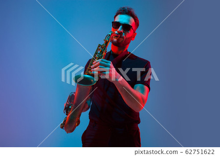 Young caucasian jazz musician playing the saxophone in neon light Young caucasian jazz musician playing the saxophone in neon light 62751622