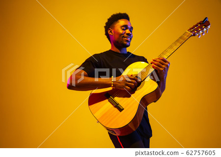 Young african-american musician singing, playing guitar in neon light Young african-american musician singing, playing guitar in neon light 62757605