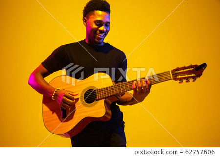 Young african-american musician singing, playing guitar in neon light Young african-american musician singing, playing guitar in neon light 62757606