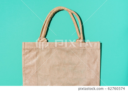 Brown cotton eco bag on blue background. Top view. Copy space. Tote reusable organic craft package. Recycle and reuse concept. Sustainable textured grossery bag Brown cotton eco bag on blue background. Top view. Copy space. Tote reusable organic craft package. Recycle and reuse concept. Sustainable textured grossery bag 62760374