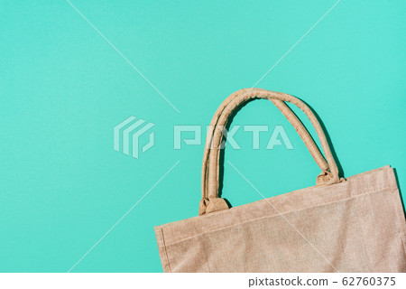 Brown cotton eco bag on blue background. Top view. Copy space. Tote reusable organic craft package. Recycle and reuse concept. Sustainable textured grossery bag Brown cotton eco bag on blue background. Top view. Copy space. Tote reusable organic craft package. Recycle and reuse concept. Sustainable textured grossery bag 62760375