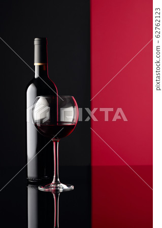 Glass and bottle of red wine on a black reflective 62762123