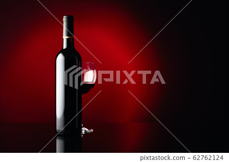 Glass and bottle of red wine on a black reflective 62762124