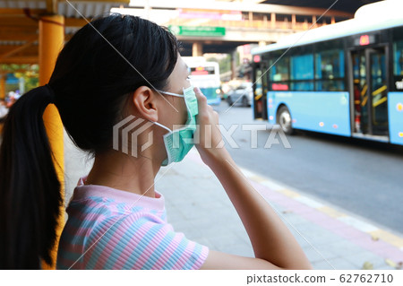 Sick asian child girl wearing protection mask against air pollution at bus stop in the city Bangkok,inhale fine dust,pm 2.5,female people using face mask to protect their health from pollution smog 62762710